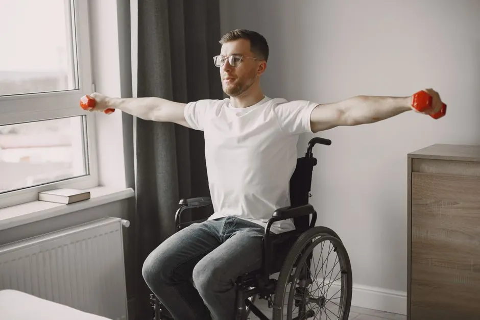Man in wheelchair lifting red dumbbells in a bright room, promoting inclusive fitness.